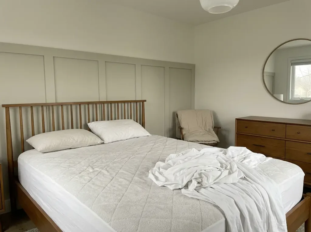 A stripped bed with sheets in a pile and the comforter still folded on the chair, mid-laundry