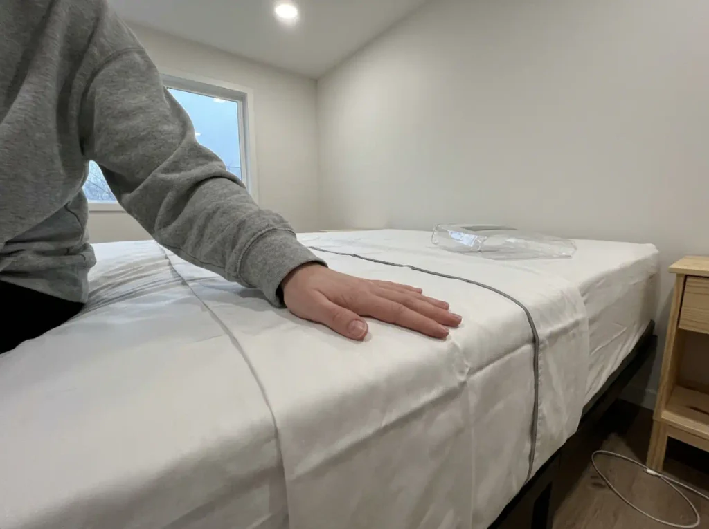 A hand running across a white sateen sheet still creased from its packaging