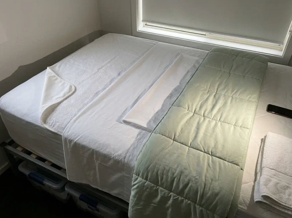 Four bedding layers laid overlapping on a stripped mattress under hard side light, each surface reading differently