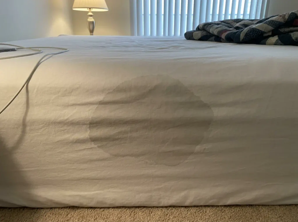 A damp patch drying on a white percale sheet, lamp raking across the weave to show the grid