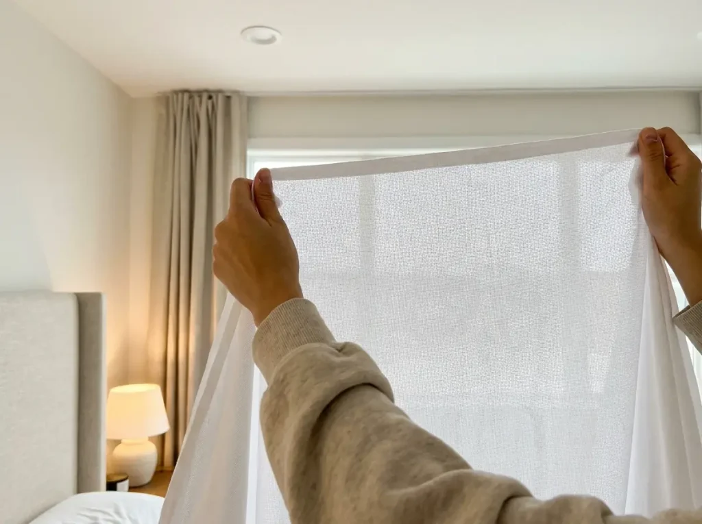 A white cotton sheet held up to a bright window, the weave grid visible as pinpricks of light