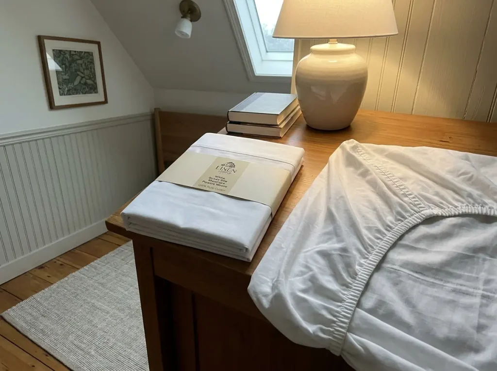 A folded percale sheet set on a nightstand with its packaging band and hem stitching in view