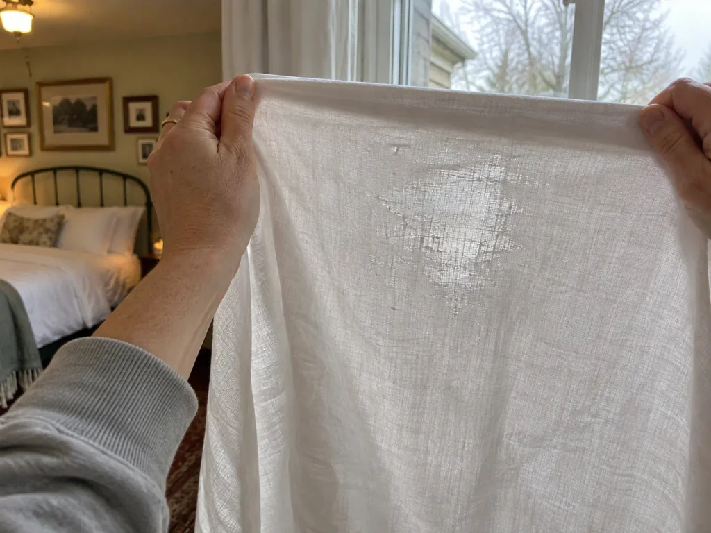 Cotton sheet held up to a window, a brighter thin patch showing through the weave
