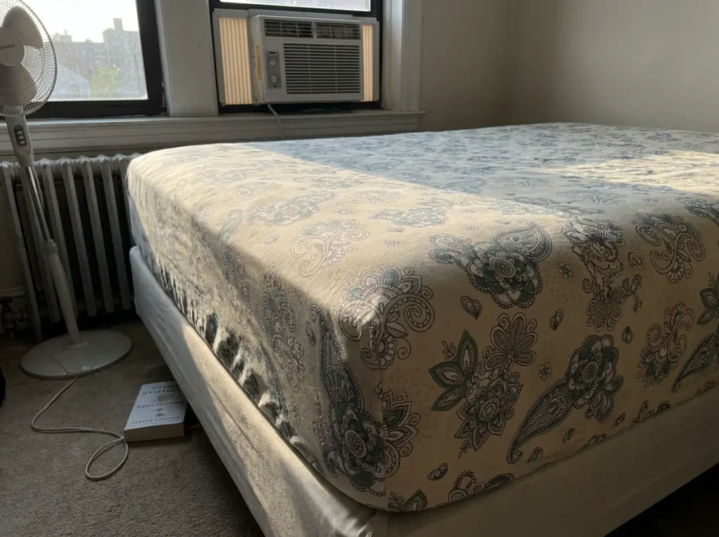 A percale fitted sheet pulled taut on a mattress, its weave lit edge-on by low afternoon sun