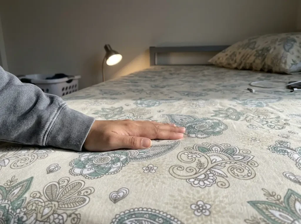 A hand smoothing an oatmeal percale sheet with lamp light raking across it to show the weave