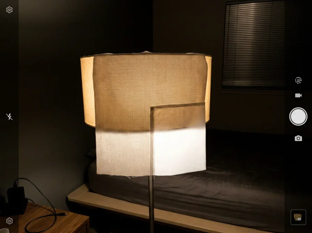Percale sheet held against a lit lamp shade, the weave grid showing through as pinholes of light