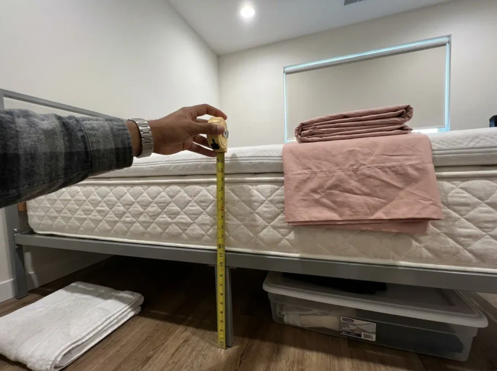 A tape measure held down the side of a bare mattress with a topper stacked on it