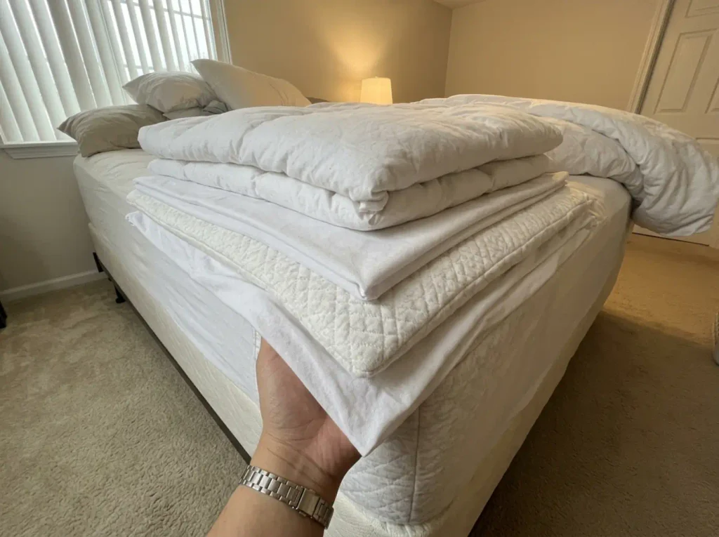 Duvet, flat sheet, fitted sheet and mattress protector peeled back in a stair-step at one corner