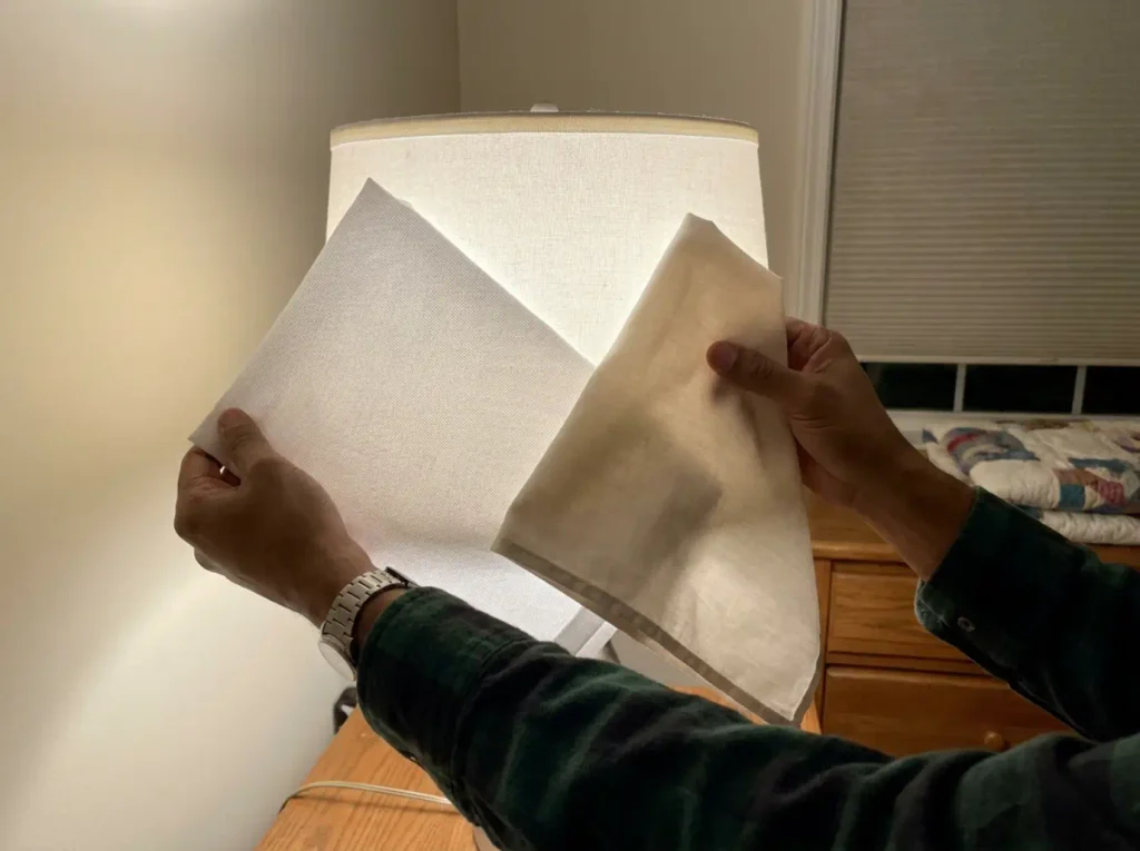 Two sheets held against a lamp showing the open percale grid beside the closed sateen surface