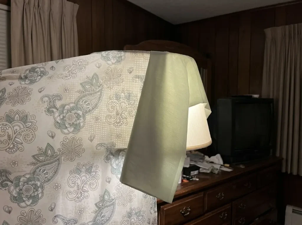 A percale sheet backlit by a lamp showing a grid of pinholes beside a sateen that glows solid