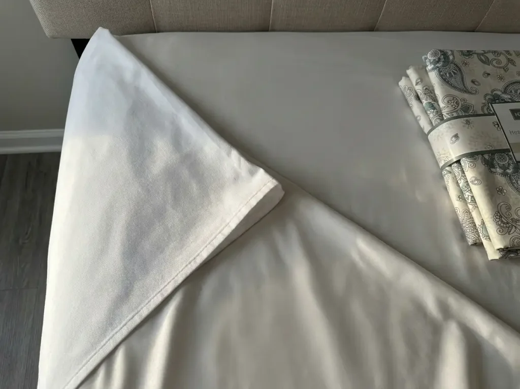 Plain percale and a cooling-marketed sheet laid overlapping on a bed to compare weave and surface