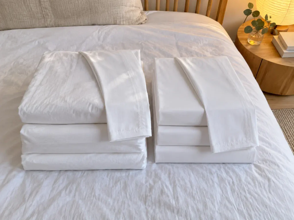 Two folded cotton sheet sets side by side on a bed, one dense and heavy, one finer and matte