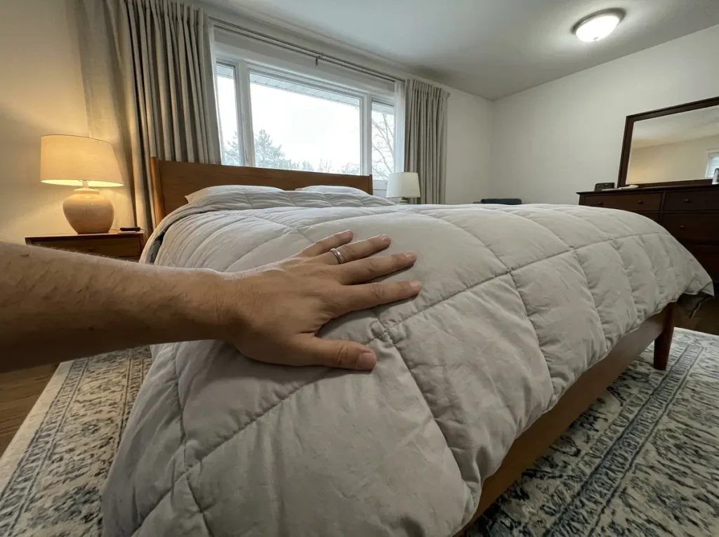 A palm laid flat across the stitched seam of a comforter where the fill pinches thin between chambers