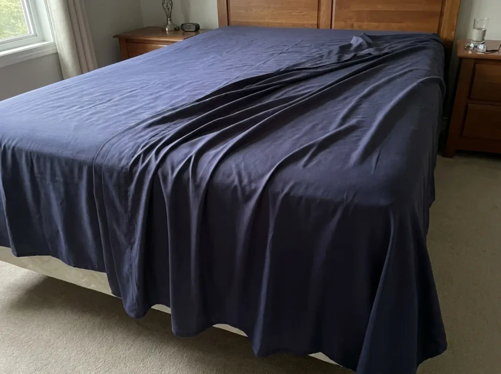 A bamboo lyocell sheet set laid across a bed in raking light showing its smooth sateen drape