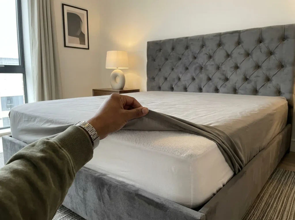 A fitted sheet peeled back off a mattress corner to show the cotton terry face of the protector underneath