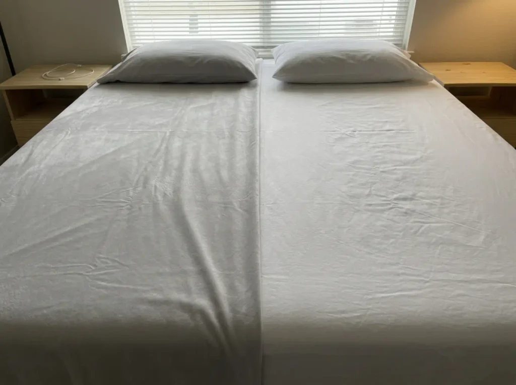 Brushed polyester and matte cotton percale laid edge to edge under a raking lamp, one glowing, one flat