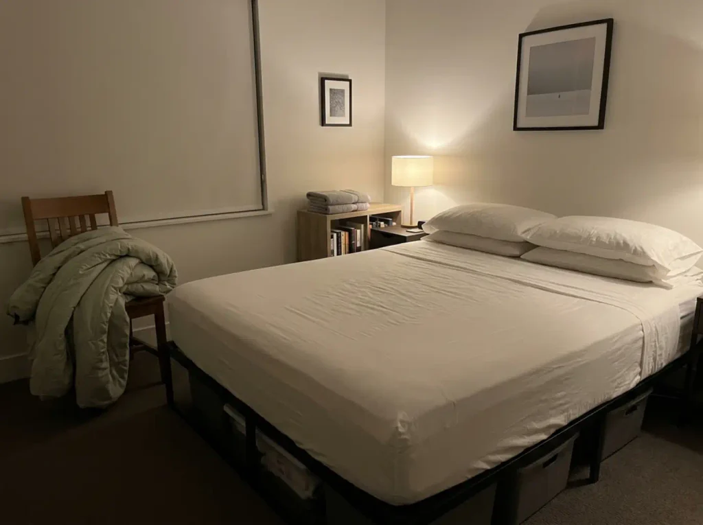 A guest bed made up with only a flat sheet at night, the comforter carried off and dumped over a chair