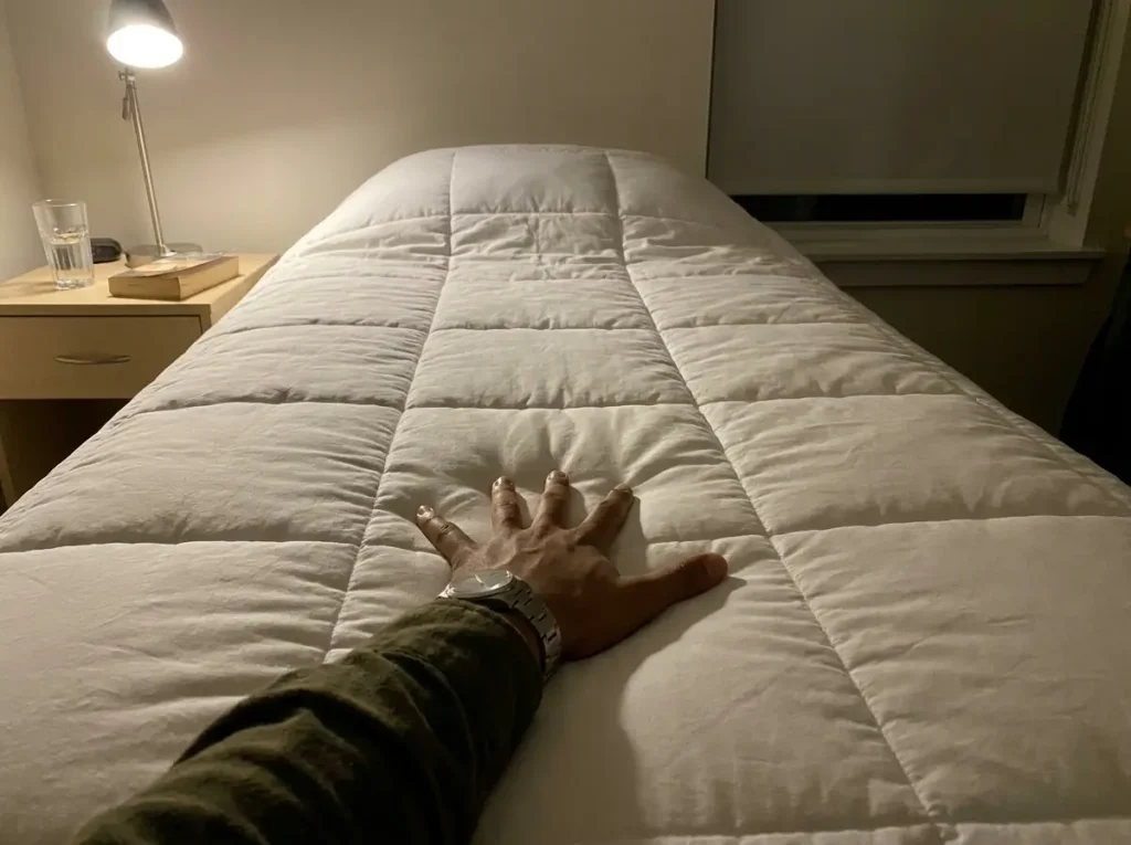 A hand pressed flat on a white percale-shell comforter, checking how long the surface stays cool