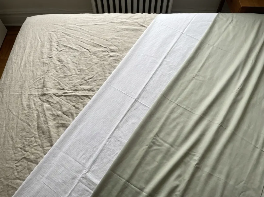 Linen, cotton percale and bamboo viscose sheets overlapping, each showing a different texture