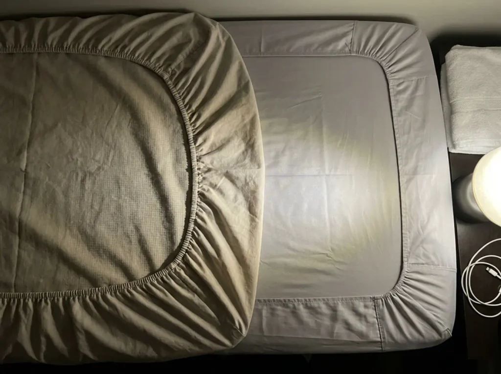 Matte percale and glossy sateen laid side by side under raking lamp light showing the weave difference