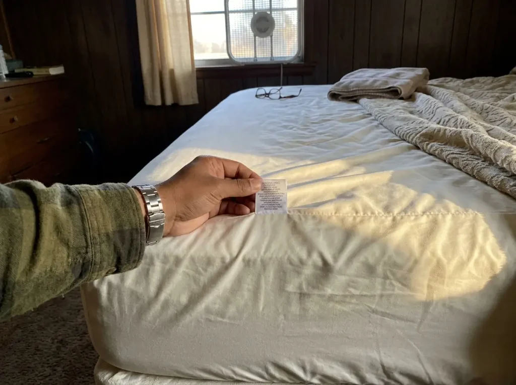 A hand turning out the care tag on the fitted sheet already on the bed to read what the fiber is