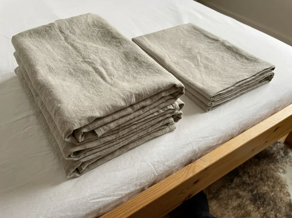 A gauzy summer-weight linen sheet folded beside a midweight one, showing the difference in body