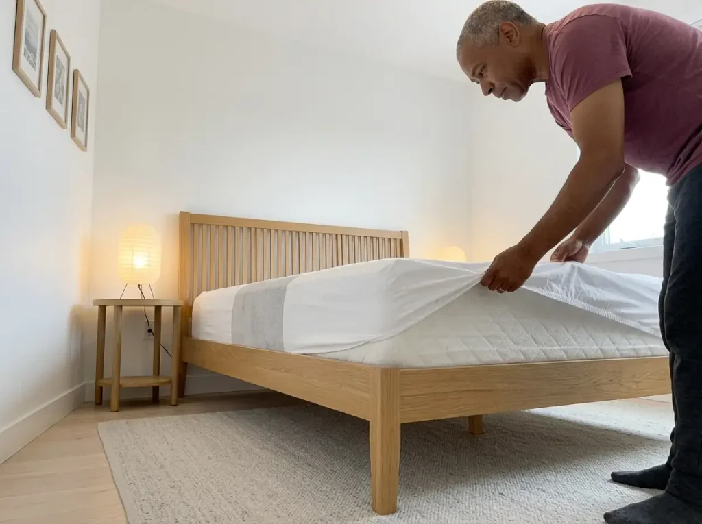 Someone stripping a worn microfiber fitted sheet off a mattress, pilling visible where the hips sit