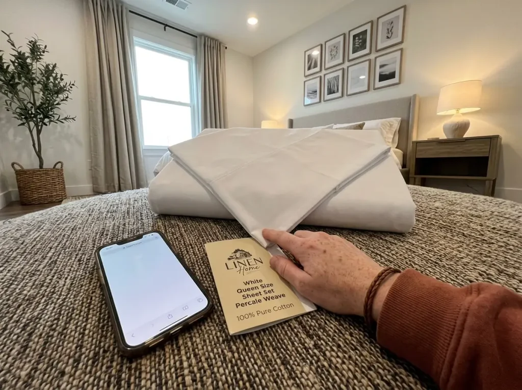 A phone held beside a sheet set's packaging card while looking up a certificate number