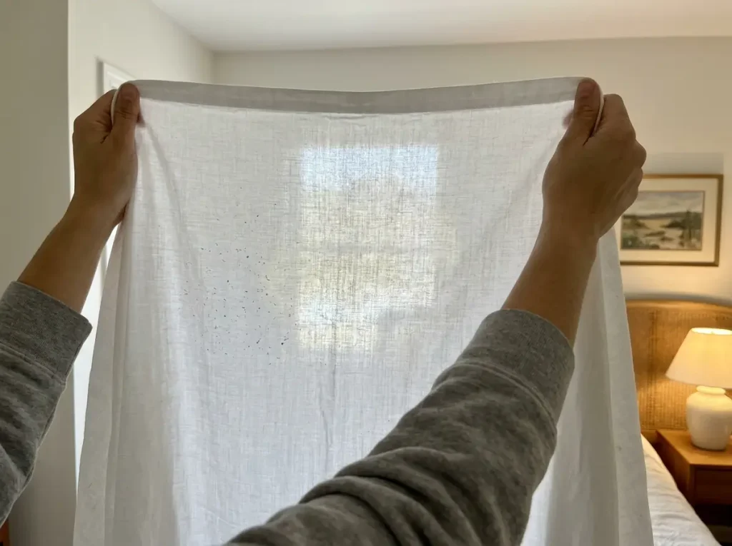 Worn cotton sheet held up to a window showing thin patches where light passes through