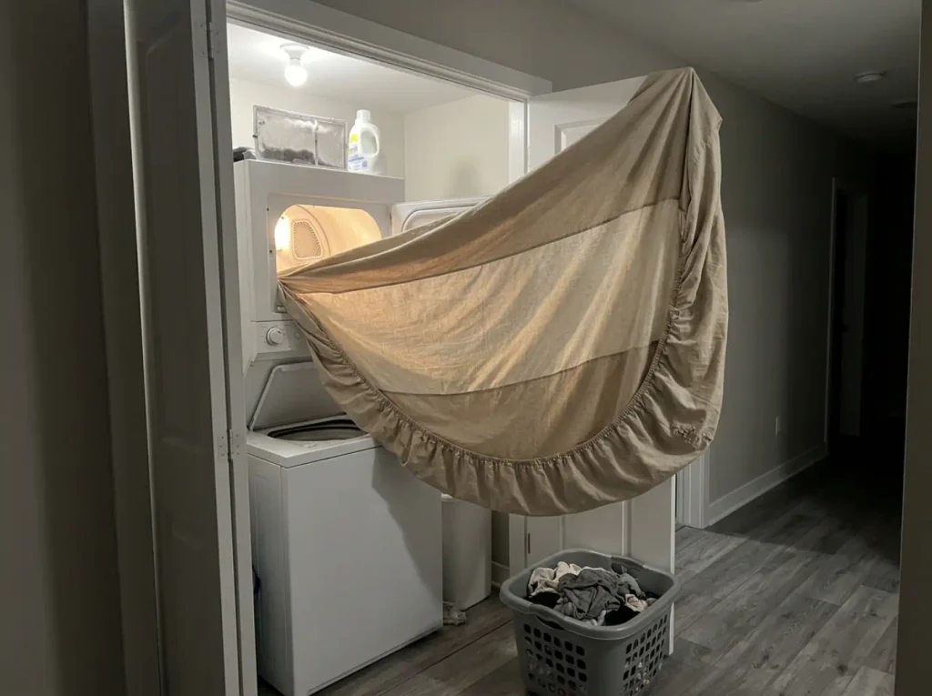 A washed percale fitted sheet held to a dryer's light, the hip band reading thinner than the corners