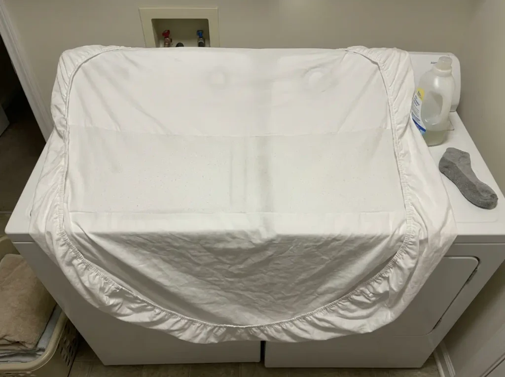 A washed white cotton sheet showing a band of pilling across the middle where a sleeper lies