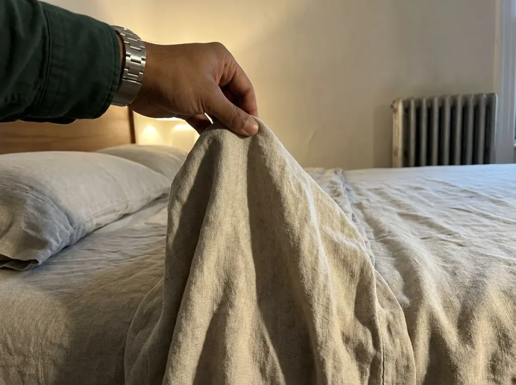 Fingers pinching a heavy French linen sheet, showing the body and weight of the fabric