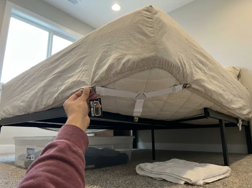 Elastic corner straps clipped diagonally across the underside of a mattress to hold the fitted sheet