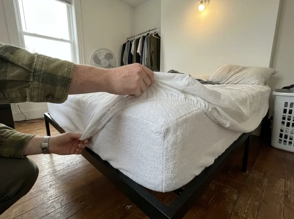 Fitted sheet peeled back off a corner to show the cotton terry mattress protector underneath
