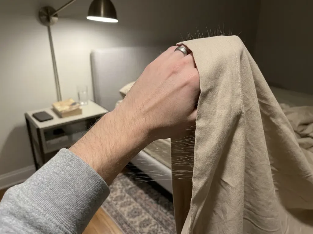 Microfiber top sheet lifted at night and clinging to itself with static under a single bedside lamp