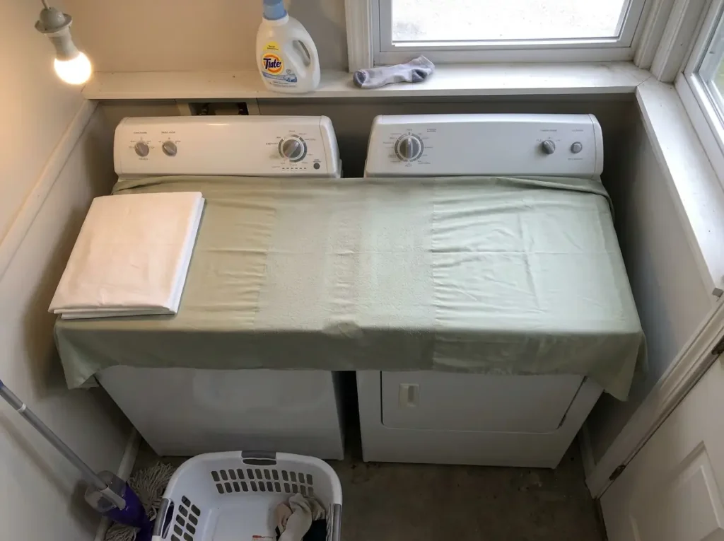 A much-washed sheet spread flat on a dryer lid, the pilled band across its middle third catching the light