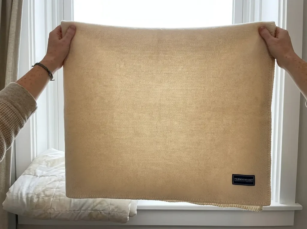 Wool blanket held against a dormer window beside a flattened comforter showing thin spots