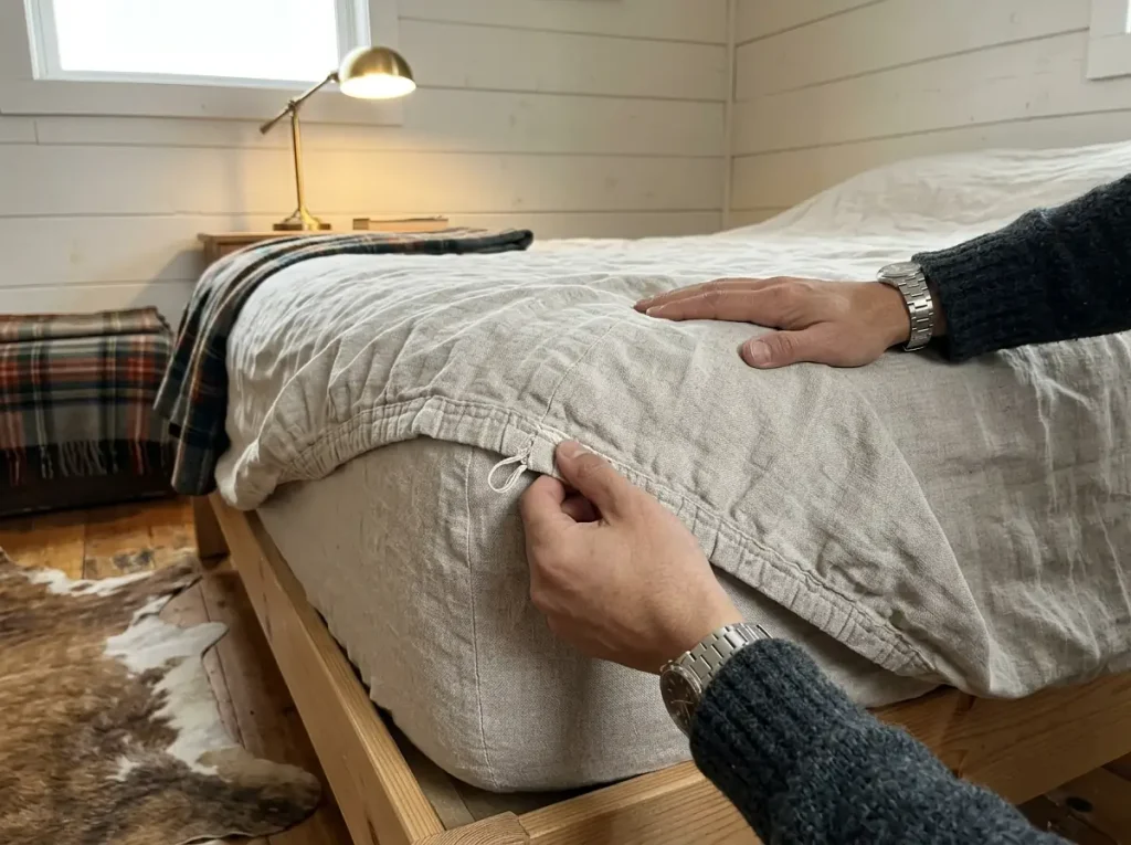 The hem stitching at the corner of a much-washed linen fitted sheet, softened and gone thin