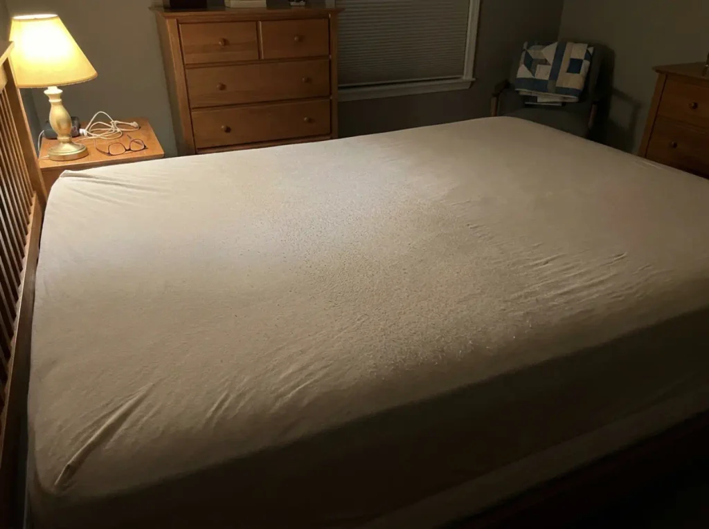 Pilling across the middle of a worn bamboo fitted sheet picked out by raking lamplight