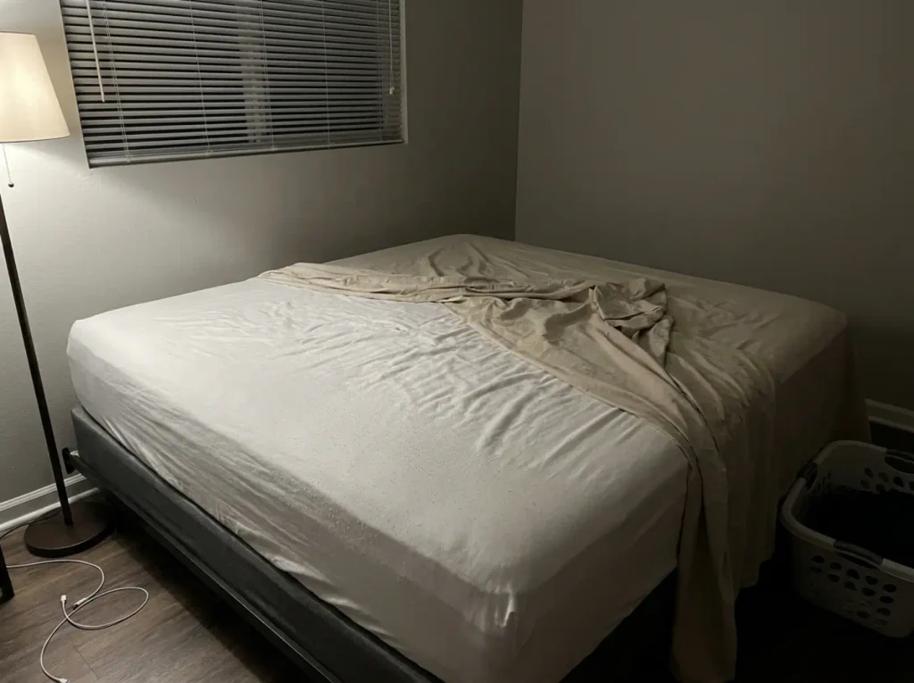 Raking lamp light across a washed sateen sheet showing a fine haze of pilling on the surface