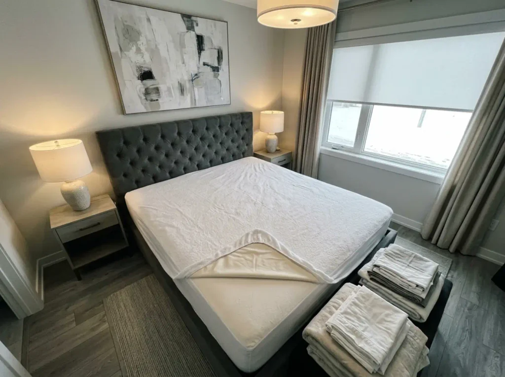 Cotton terry mattress protector alone on a stripped bed, corner turned back to show the backing