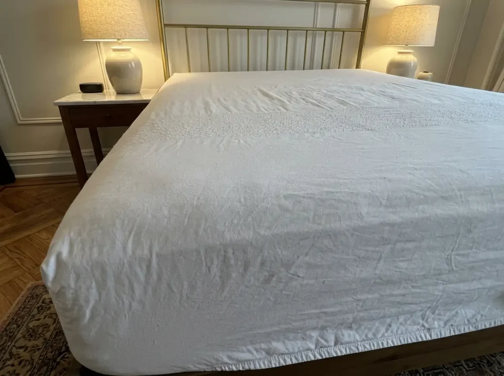 A fitted sheet on a bed under raking lamplight, the worn band across its middle third showing pilling