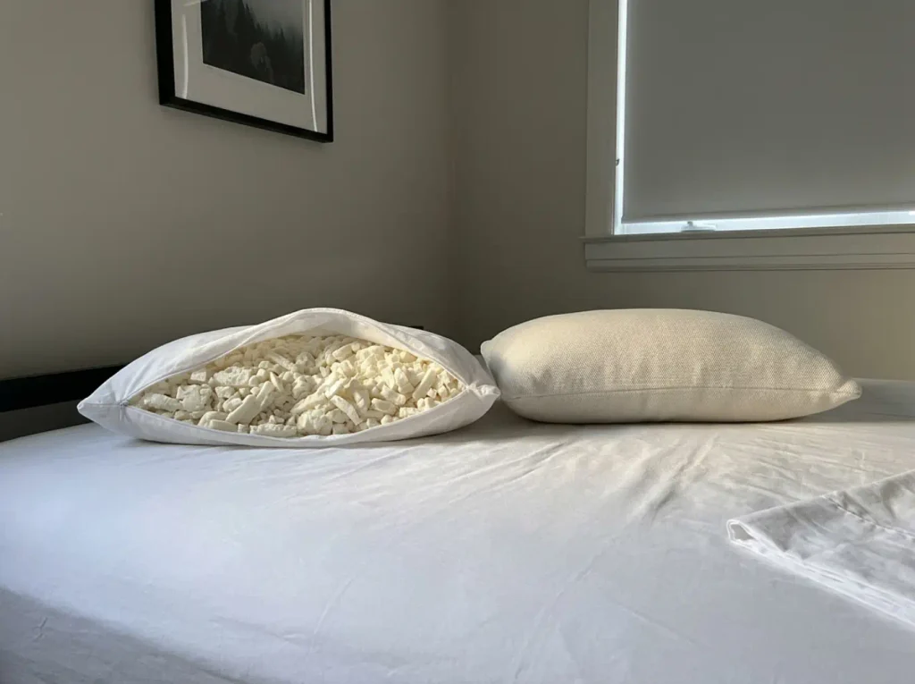 A shredded latex pillow beside its unzipped cotton protector at the head of a bed in low afternoon light