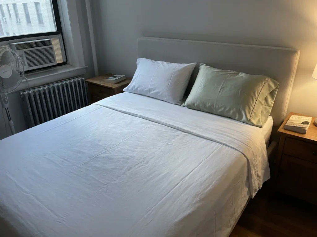 One made bed with two different pillowcases, a crisp white one and a smooth sage one