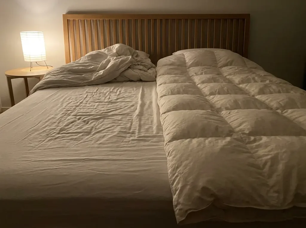 A bed at night with two separate duvets, one thrown back and one still flat, on a shared fitted sheet