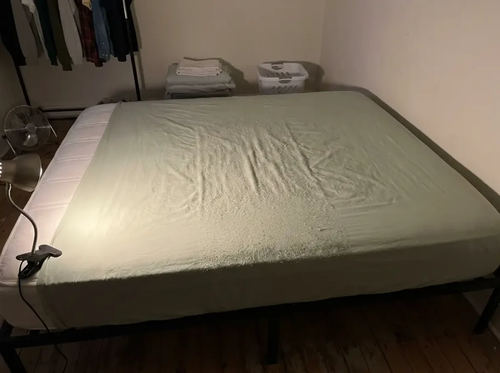 A washed sheet spread flat with a pilled band across its middle third raked by a low lamp
