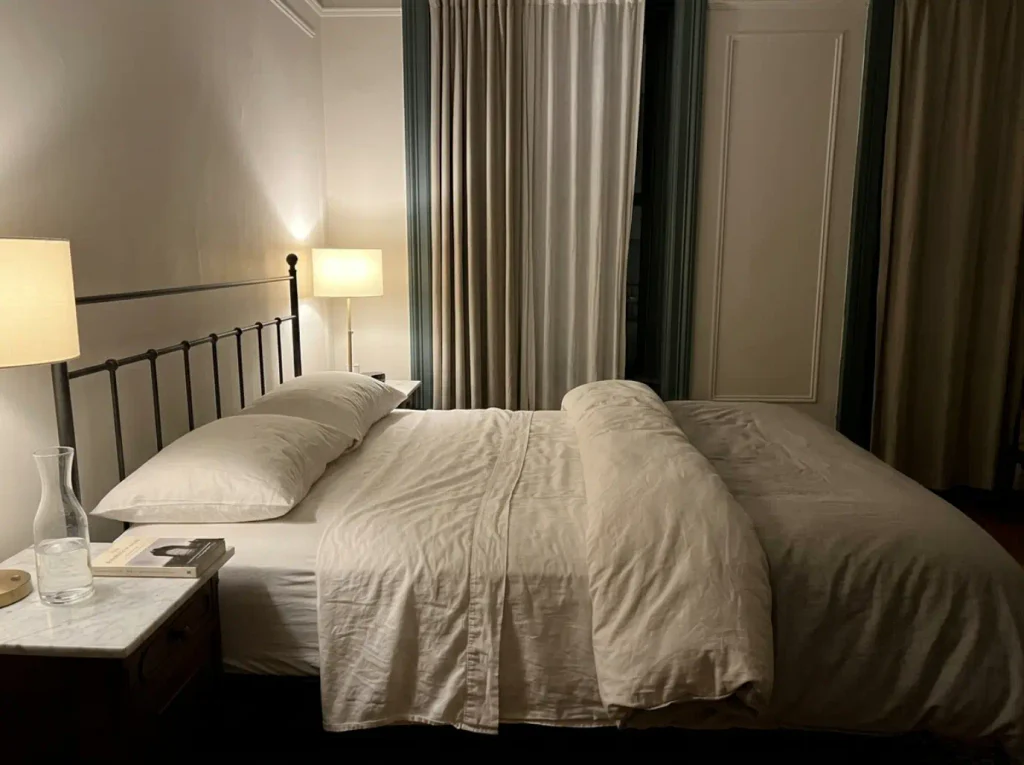 A duvet pushed to one side of the bed at three in the morning, lit by a single bedside lamp
